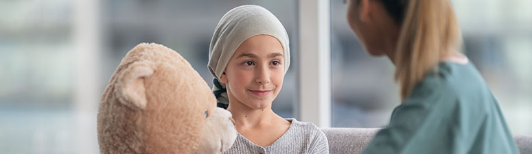 Child with cancer holding teddy bear looking at therapist
