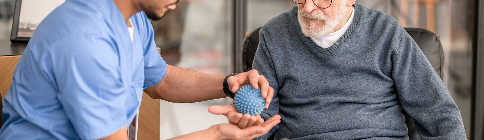 Therapist helping patient hold a ball during a hand exercise