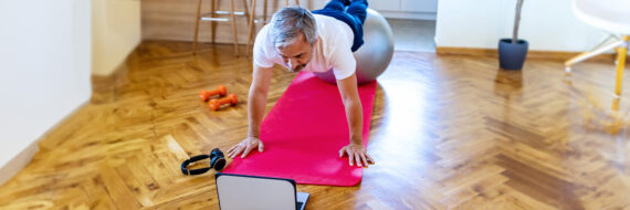 Person stretching on yoga mat in front of laptop