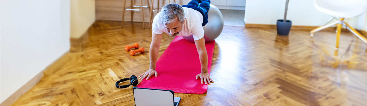 Person stretching on yoga mat in front of laptop