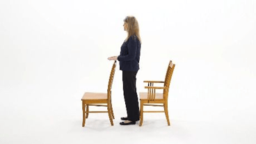 A woman stands between two wooden chairs with arms out, symbolizing balance and focus in medbridge healthcare education.