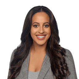 A smiling person with wavy brown hair and a plaid blazer against a white background, used for medbridge profile.