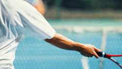 A tennis player in a white shirt is hitting a yellow ball with a racquet on a blue court.