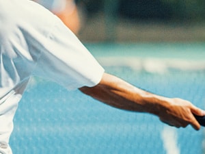 A tennis player in a white shirt is hitting a yellow ball with a racquet on a blue court.
