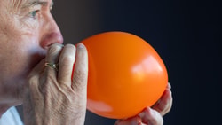 Someone in a white shirt blows up an orange balloon.