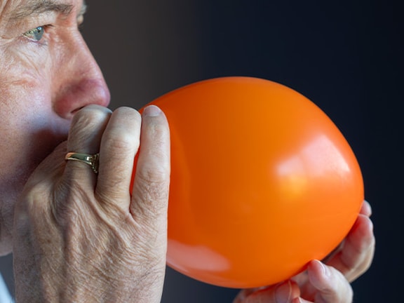 Someone in a white shirt blows up an orange balloon.
