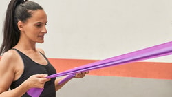 User exercises with a purple resistance band fixed to a pillar in the medbridge app.