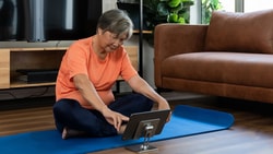 A person on a blue yoga mat in the living room uses a tablet with medbridge on it.