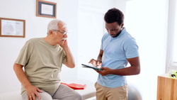 Clinician reviewing remote therapeutic monitoring (RTM) updates on tablet with older patient in outpatient clinic