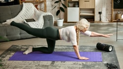 Older adult performing bird-dog exercise on yoga mat at home as part of patient engagement activities for chronic low back pain rehab.
