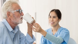 Speech-language pathologist assisting an older adult with safe swallowing using a cup during a therapy session.