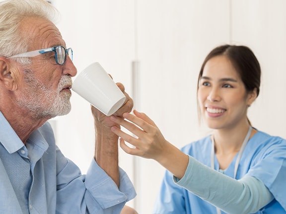 Speech-language pathologist assisting an older adult with safe swallowing using a cup during a therapy session.