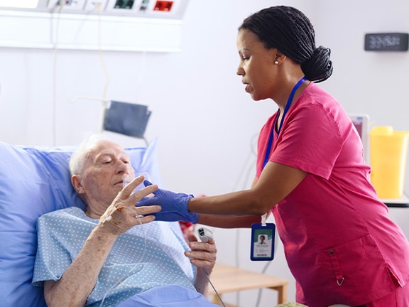 Speech-language pathologist in pink scrubs assisting an elderly patient in an ICU hospital bed, providing attentive care.