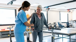 A healthcare worker helps an elderly woman walk at a Medbridge rehab center.