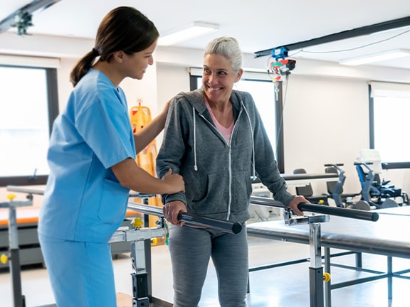 A healthcare worker helps an elderly woman walk at a Medbridge rehab center.
