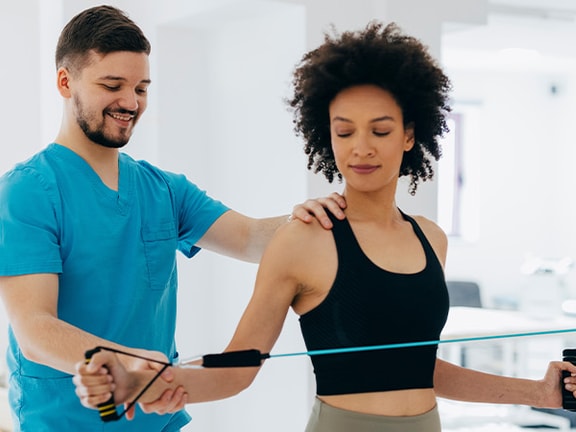 Physical therapist guiding a patient through resistance band shoulder exercises in a bright rehabilitation clinic.