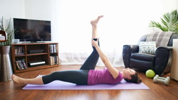 Person performing a supine hamstring stretch on a yoga mat at home to improve flexibility and stability for EDS or HSD.
