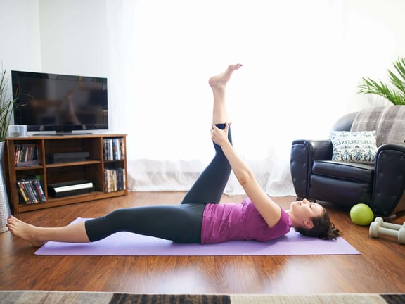 Person performing a supine hamstring stretch on a yoga mat at home to improve flexibility and stability for EDS or HSD.