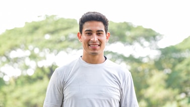 A man in a white t-shirt smiles outdoors, with green trees behind him, representing medbridge digital healthcare.