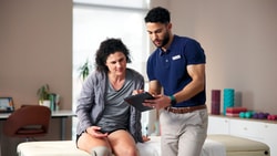 A physical therapist reviews outcomes data on a tablet with a patient during a clinic session.