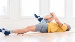 Individual in a bright room stretching on a mat with one leg bent in a Medbridge course.