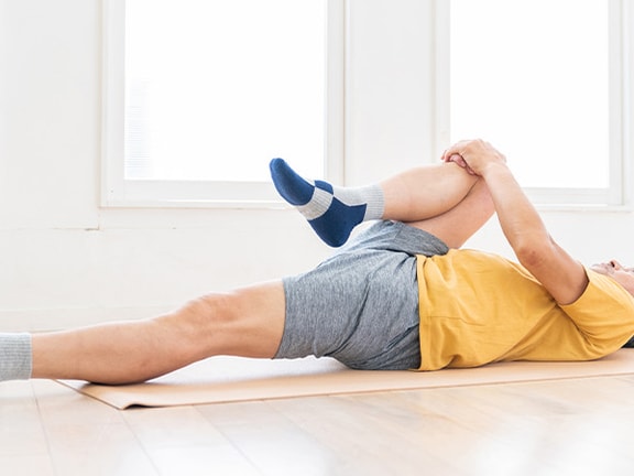 Individual in a bright room stretching on a mat with one leg bent in a Medbridge course.