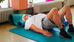 A person exercises on a teal mat in a room with radiators and potted plants.