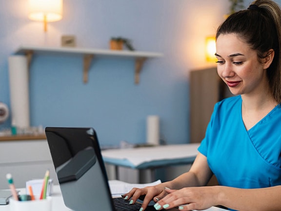 A Medbridge user in scrubs types on a laptop at a medical desk.