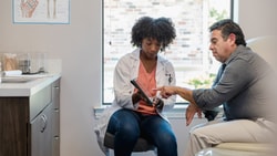 Clinician and patient review a digital treatment plan on a tablet, illustrating hybrid care in a rural clinic setting.