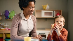 A woman and child smile at a table with toys in a playroom.