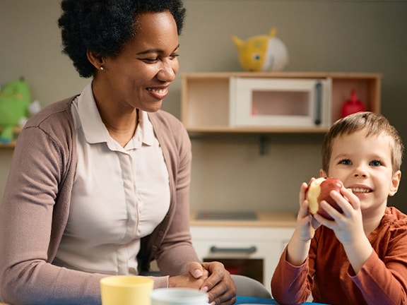 A woman and child smile at a table with toys in a playroom.