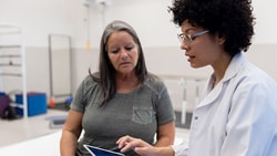 A healthcare professional uses a tablet to discuss information with a woman in a physical therapy setting, featuring medbridge.