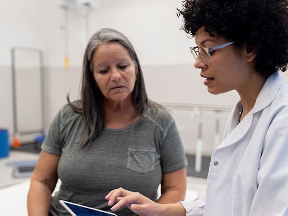 A healthcare professional uses a tablet to discuss information with a woman in a physical therapy setting, featuring medbridge.