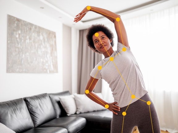 Individual stretching with motion-tracking overlay by a black sofa, reaching one arm overhead; Medbridge software visible.