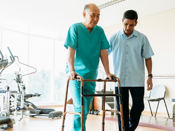 A healthcare professional helps an elderly man using a walker in a medbridge facility.