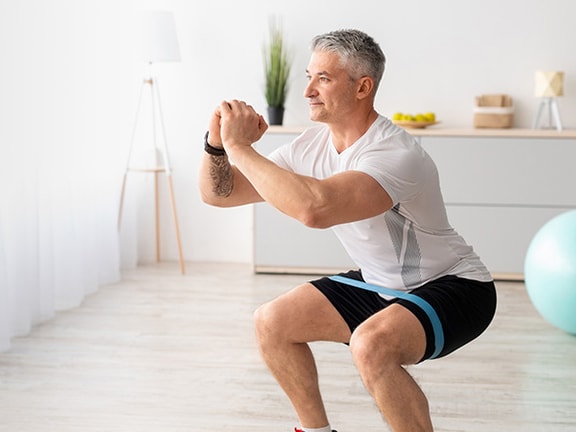 Man squatting in bright living room with yoga ball and shelves.