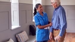 A medbridge staff member helps an elderly man with a cane in a room with benches.