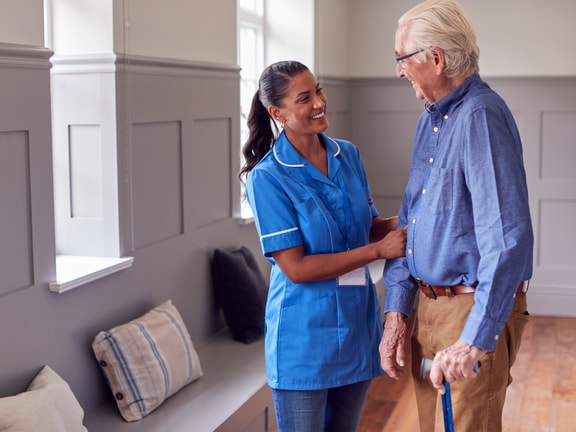 A medbridge staff member helps an elderly man with a cane in a room with benches.
