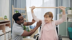 Therapist guiding a patient through a neuro rehab carryover shoulder mobility exercise with a dowel rod.