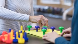 Two people using colorful peg pieces for therapy at a table, as seen on medbridge.