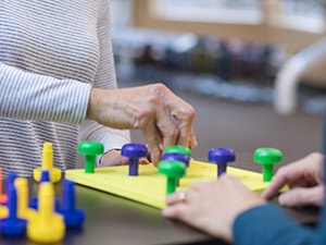 Two people using colorful peg pieces for therapy at a table, as seen on medbridge.
