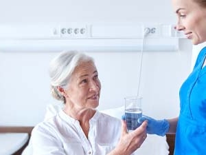 Nurse in blue scrubs standing by an elderly woman holding a water glass at medbridge.
