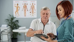 Two people in a medical office discuss a tablet next to an anatomy diagram; this is a medbridge image.