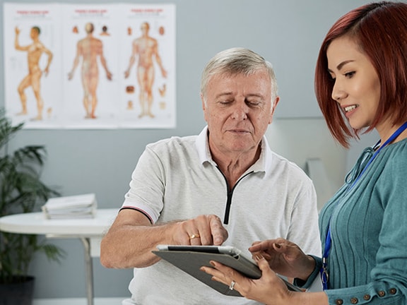Two people in a medical office discuss a tablet next to an anatomy diagram; this is a medbridge image.