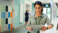 A person reads a tablet in a hallway with colorful lockers and a blurred figure behind them, representing medbridge.