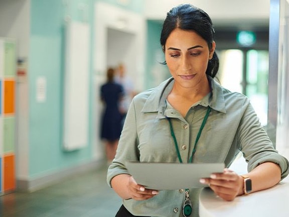 A person reads a tablet in a hallway with colorful lockers and a blurred figure behind them, representing medbridge.