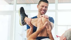 A Medbridge exercise session shows a man assisting another in stretching his leg.