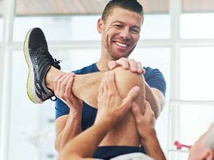 A Medbridge exercise session shows a man assisting another in stretching his leg.
