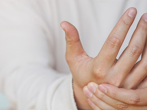A person in a light shirt clasps their left hand, set against a plain backdrop.
