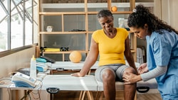 A medical professional bandages a woman's knee at a medbridge clinic.